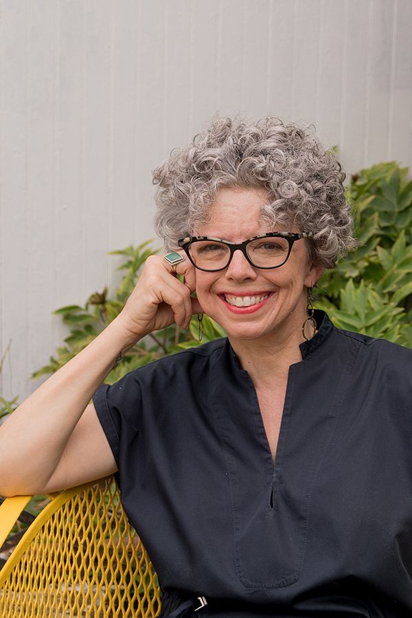 photo of a white woman with curly, grey short hair and glasses, smiling while outdoors