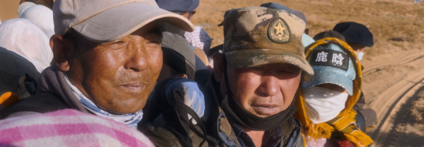 In a desert landscape, three people wearing hats and scarves in close up