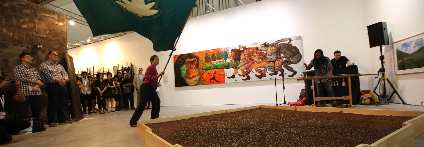person with tan skin waving a large green flag next to a garden bed inside a museum gallery