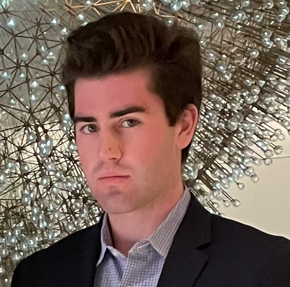 headshot of man in dark suit and in front of a large, spherical light fixture