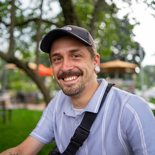 man in baseball hat outside, in front of a tree