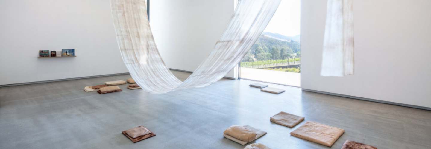 museum gallery with a large, light fabric loosely draped from the ceiling and tannish floor cushions underneath 