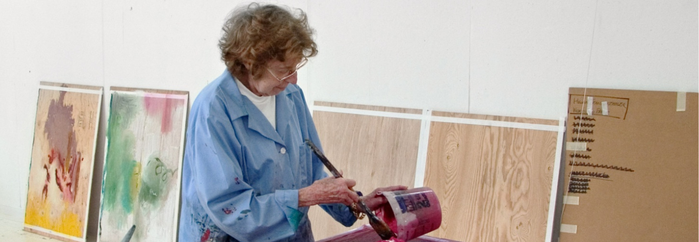 photograph of a white woman working on an artwork on a table in front of her