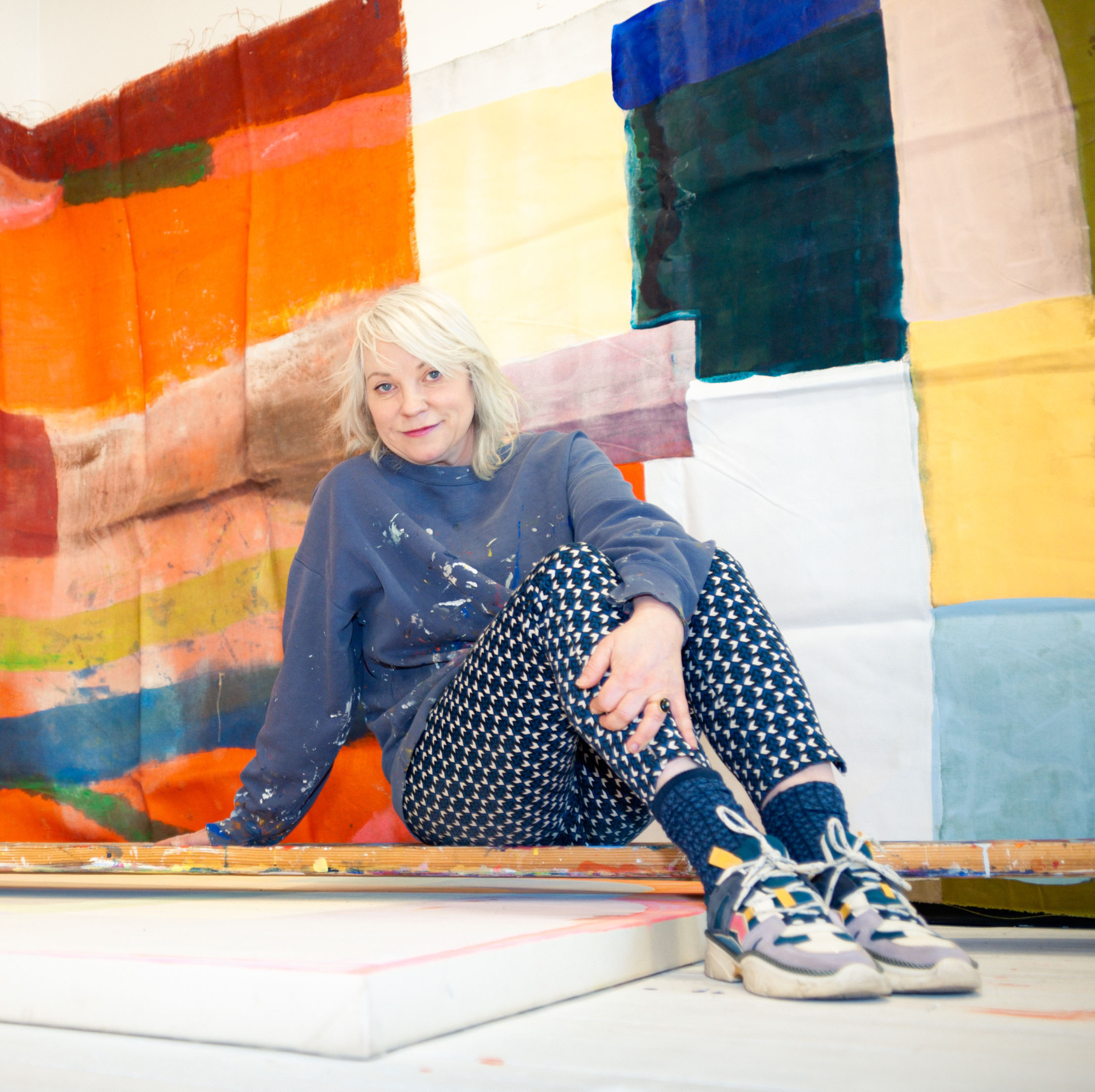 white woman with bleached hair sitting in front of an artwork in process 