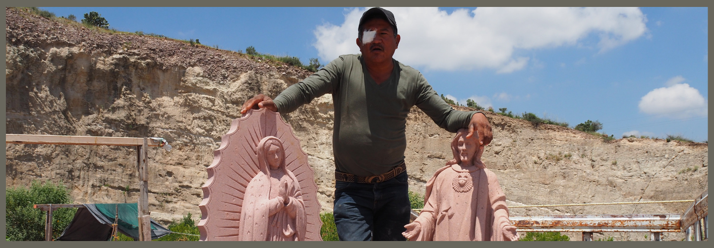 photo of a carver standing with two sculptures of Christian religious figures 