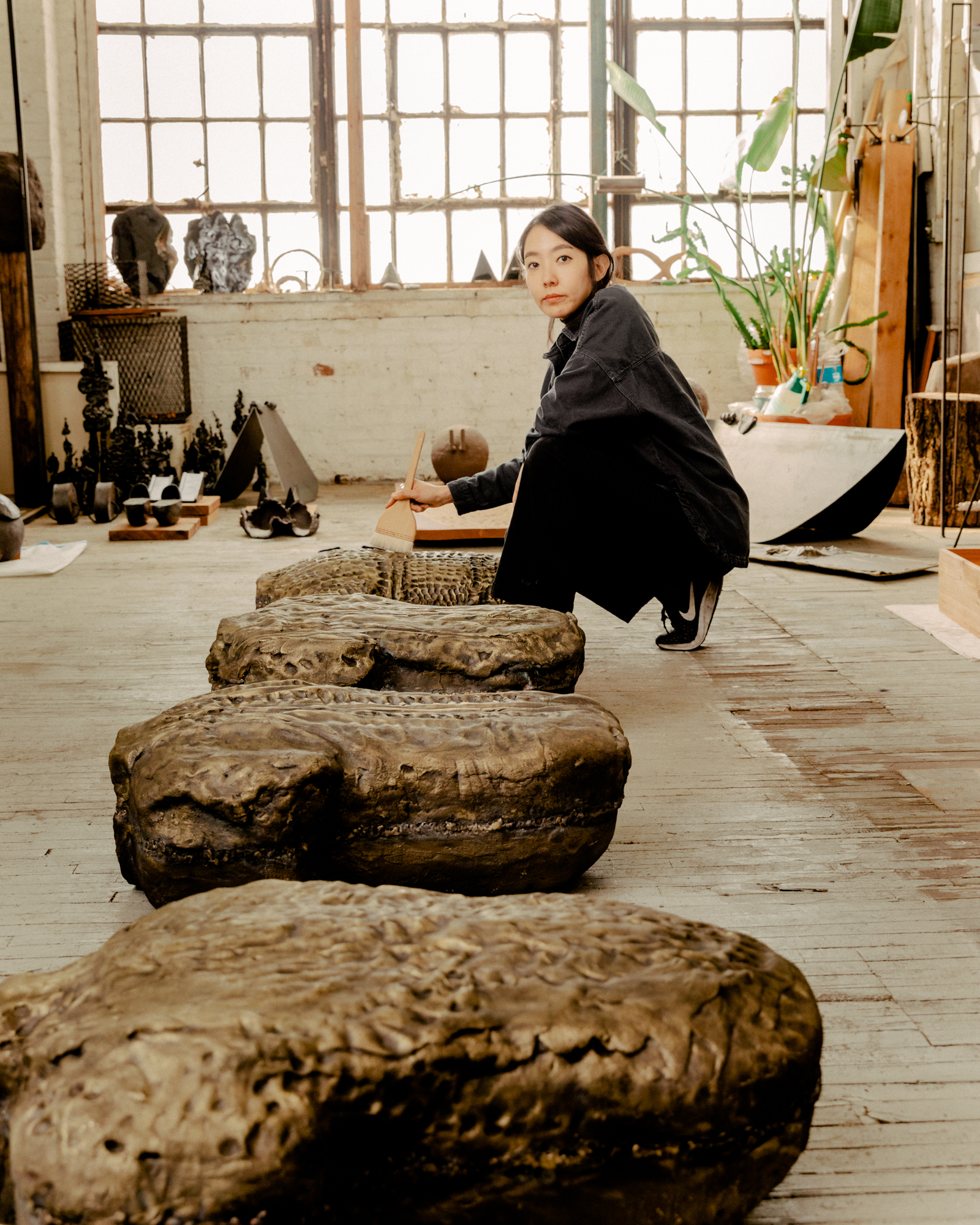 Korean woman crouching in front of brass sculptures on the ground