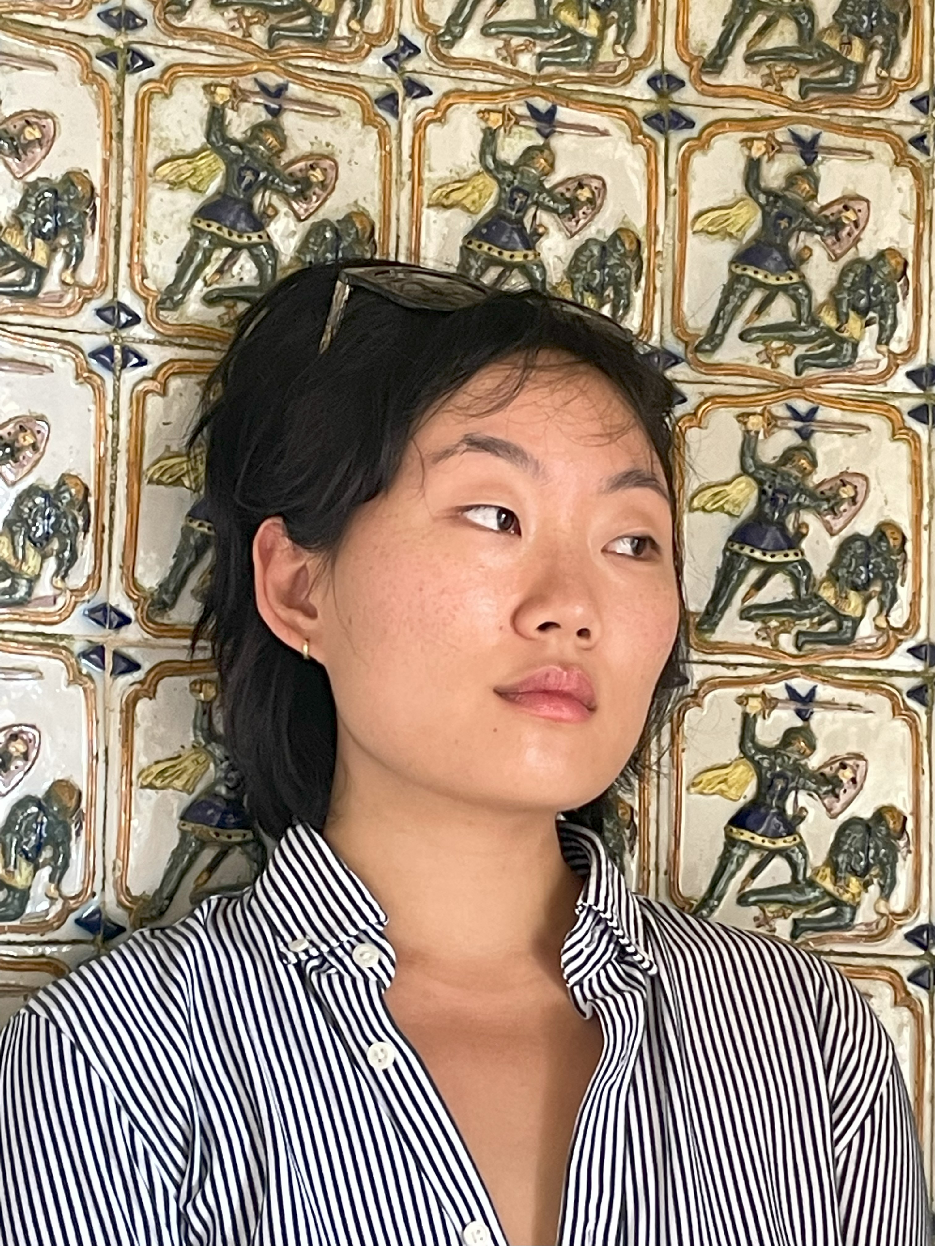 Korean woman in striped button down in front of a tile wall 