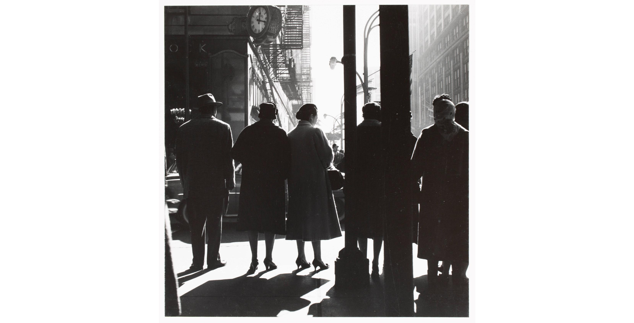 rear view of silhouetted figures in sunlight on street corner