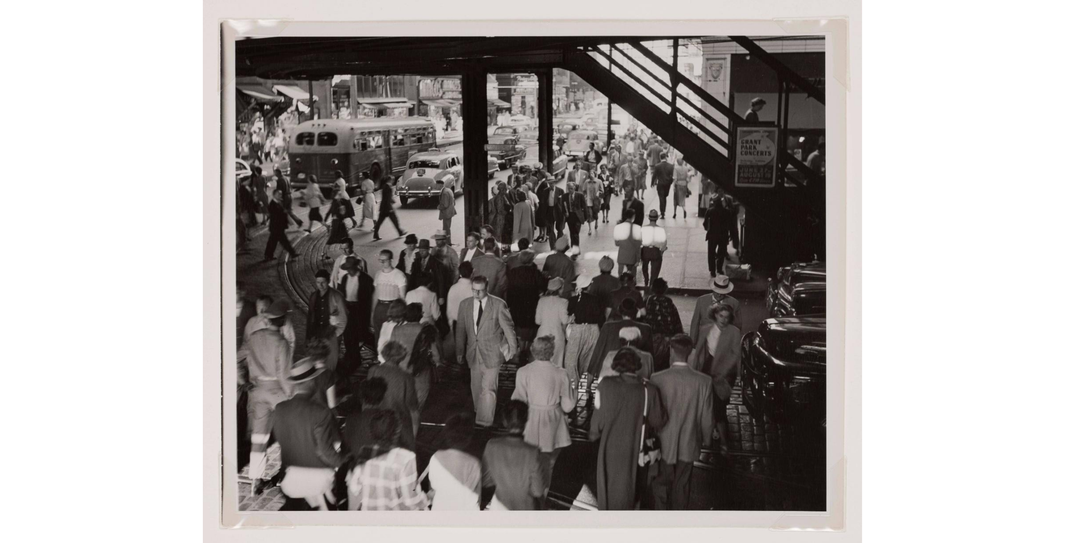 Black and white photo of pedestrian crowd walking under elevated train tracks