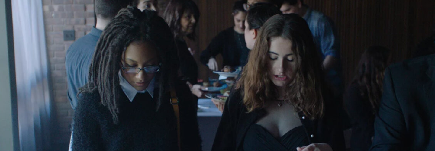 Two young women, one with light skin tone and one dark skin tone, wearing black clothing put food on plates decorated with the Star the David.