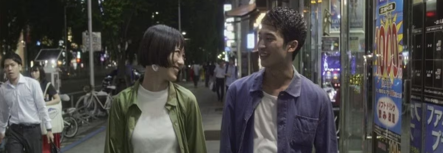 A young couple walks down a city street at night
