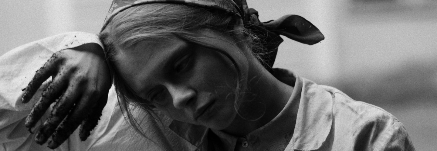 Black and white close up of a young woman wiping her brown with a hand covered in soil