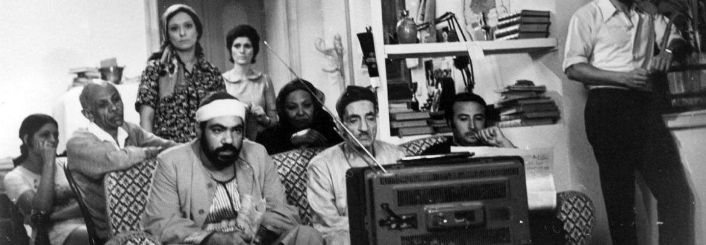 Black and white image of people seated in a living room watching a TV