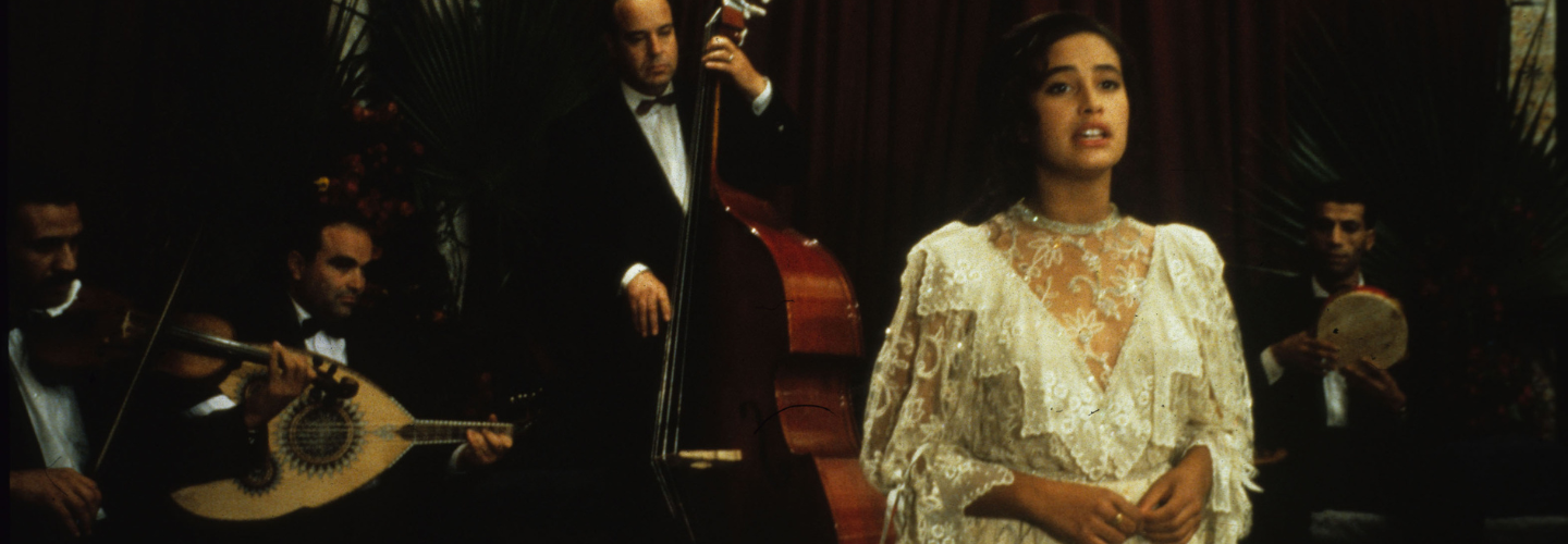 A woman in a white gown sings on a stage