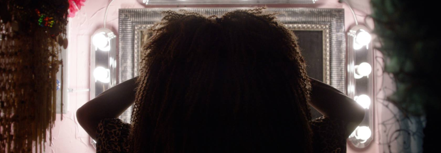 Silhouette of a person with curly hair in front of a well lit stage mirror