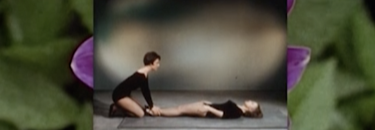 Two women in black leotards stretch in the center framed by purple flowers and foliage