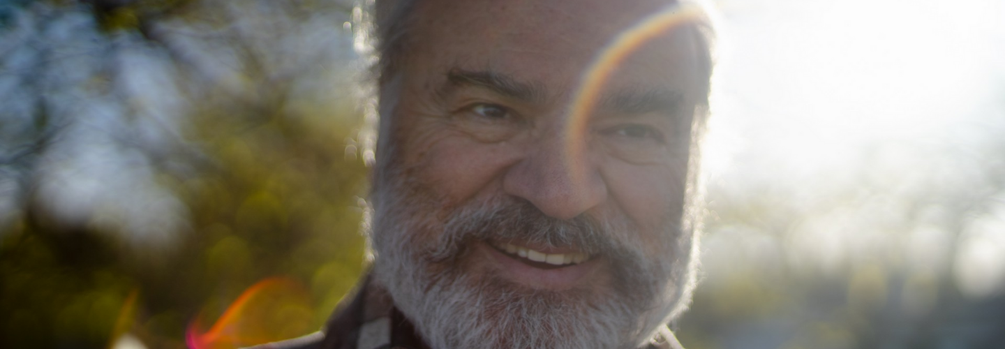 Close up of an older adult man smiling with a burst of light across his face
