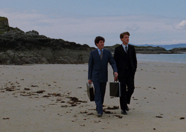 Two men in suits walking on a beach