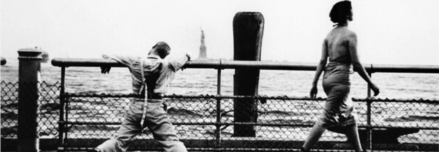 A man in broken suspenders is slumped over a railing, facing out across the 