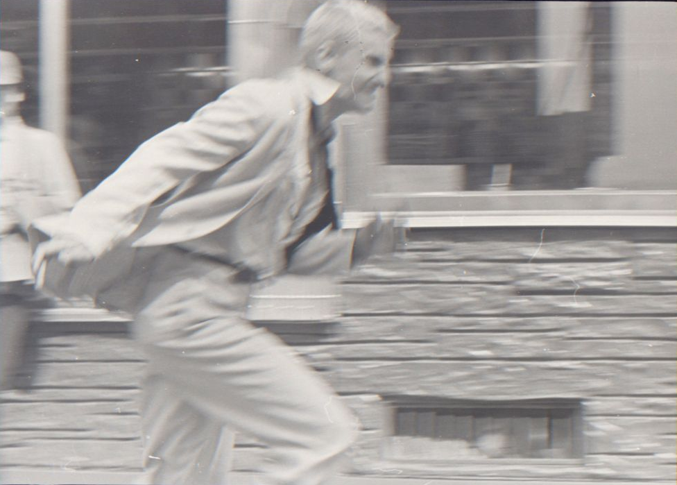 A blurry photograph of a man in a white suit running