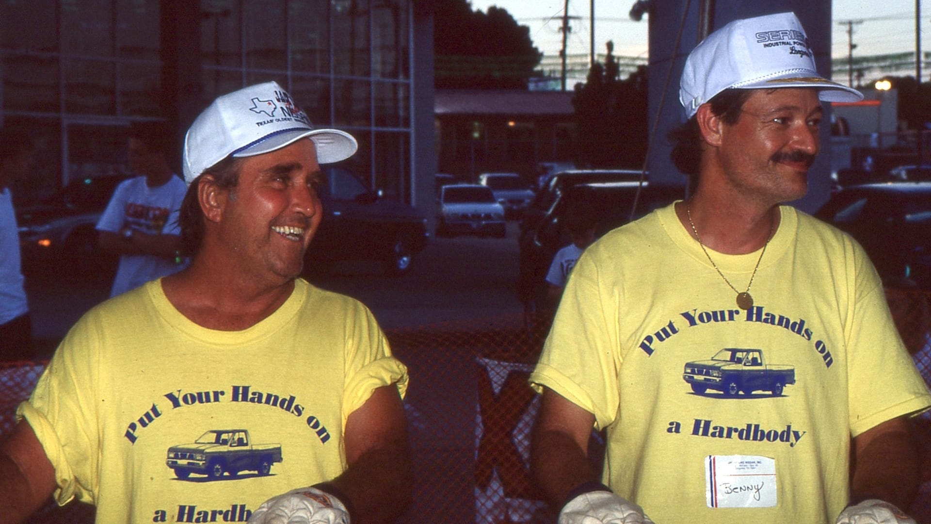 Two men in yellow shirts reading "Put Your Hands on a Hardbody"