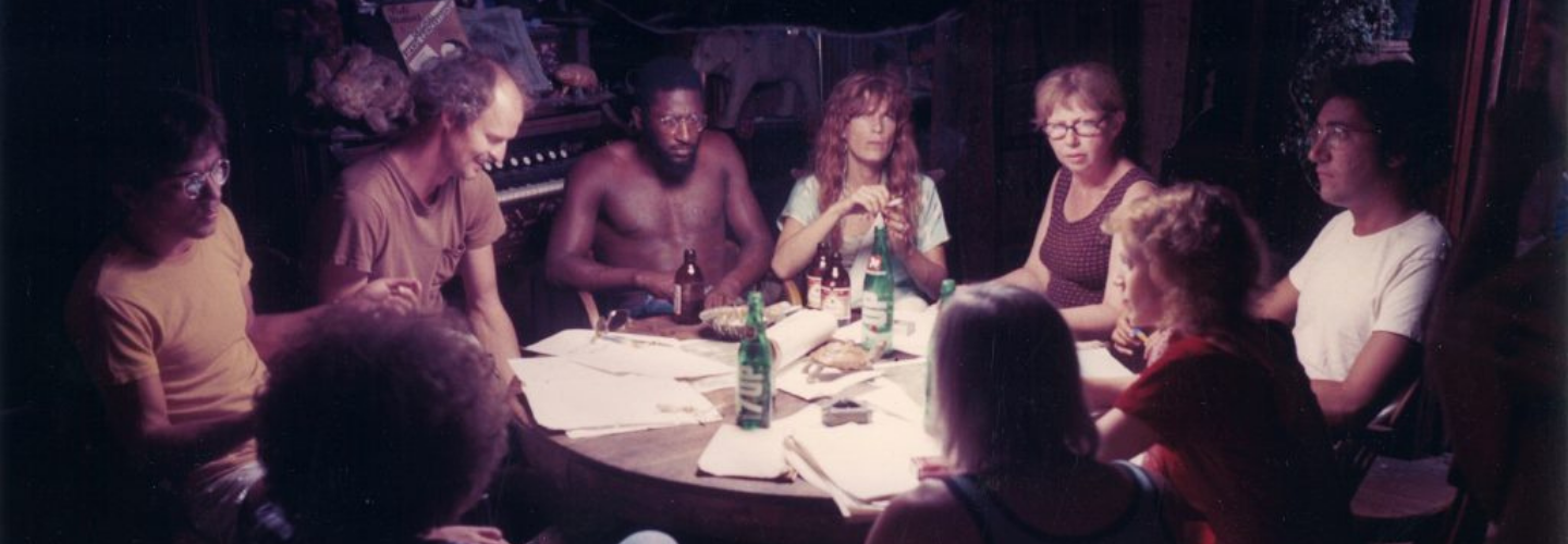 A group of people gather in discussion around a well lit table at night