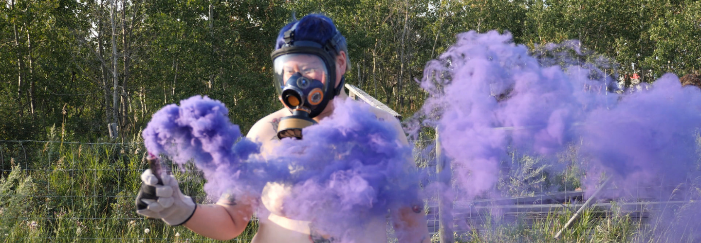 A person wearing a gas mask holding a canister that trails purple smoke