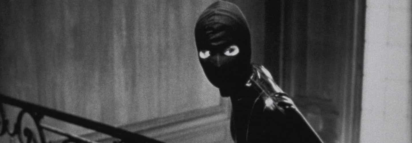 A masked, black-clad figure looks warily to the right.