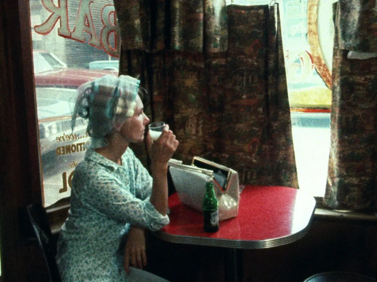 Woman in hair rollers sits at a table having a beer