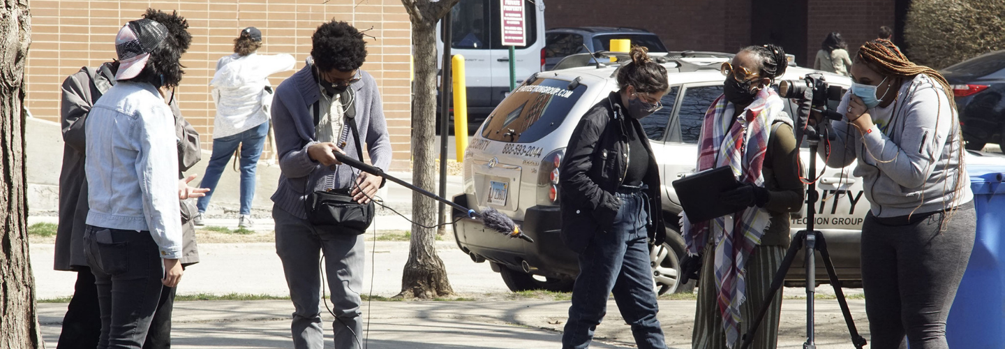 A small group of people with filmmaking equipment at work on a busy street 