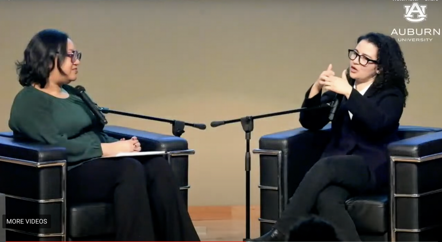 Two women sit conversing in chairs on stage