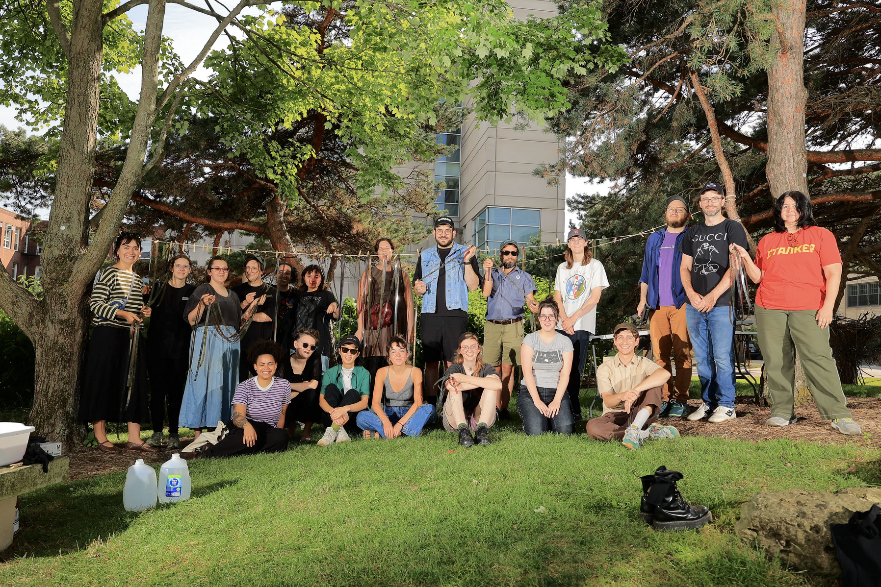 A group of people stand between two trees on a grassy slope. A clothesline between the two trees holds drying strips of film