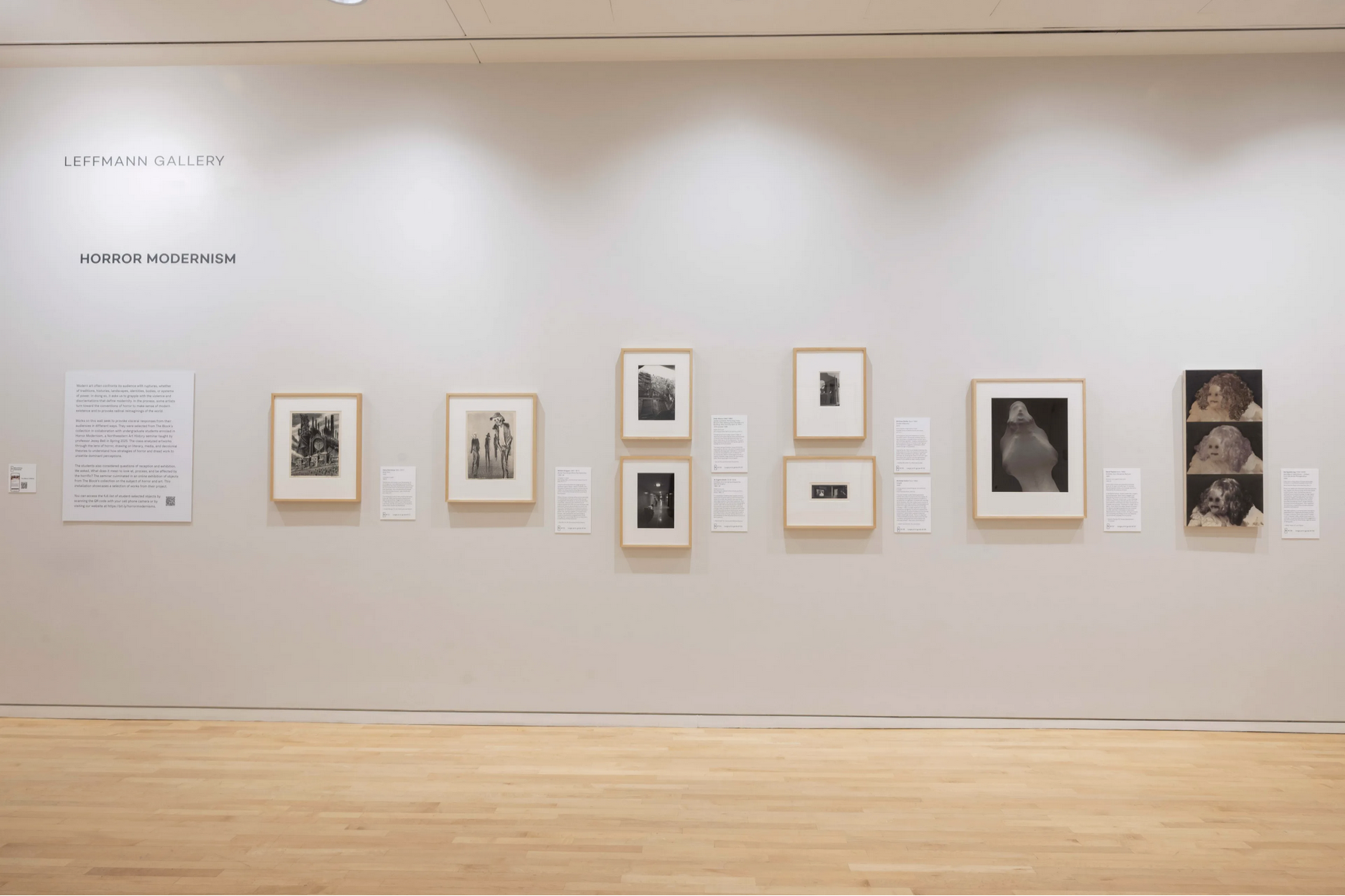 Row of artworks hang on white wall in museum gallery