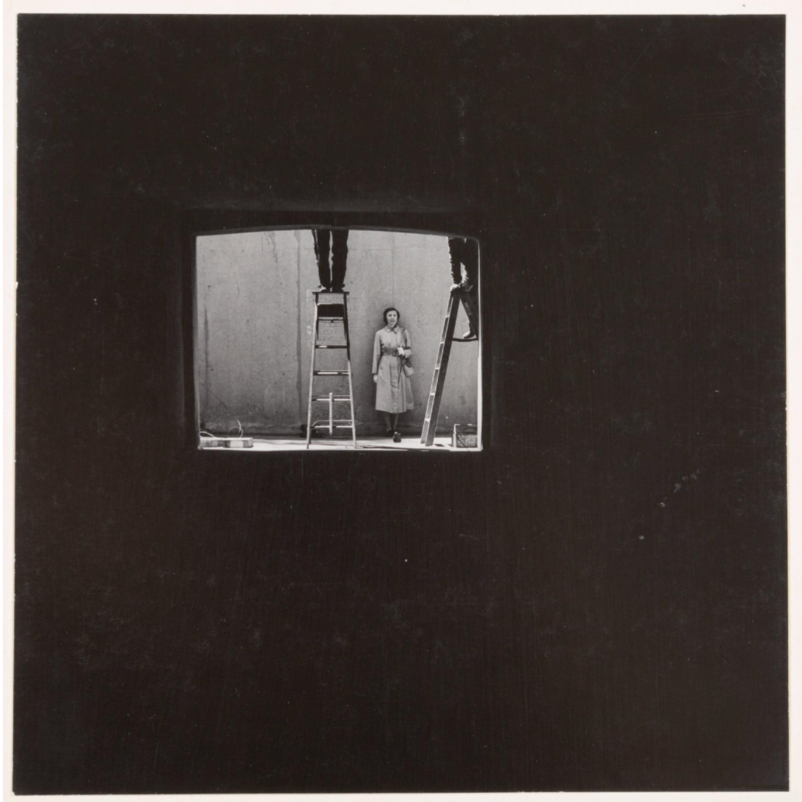 Woman stands between two ladders. Figures stand on ladders but only their legs are visible in the frame.