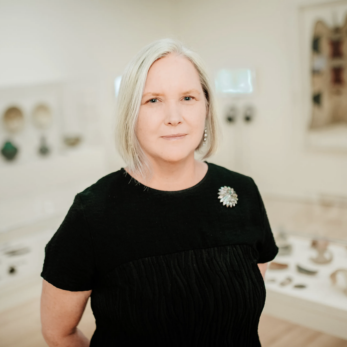 Kathleen Bickford Berzock stands solo in museum gallery with glass display cases in background