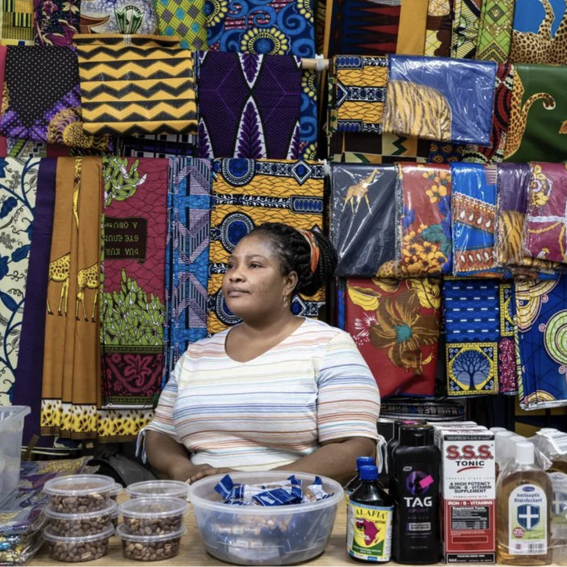 Woman sits at table in front of backdrop of various hanging patterned fabrics