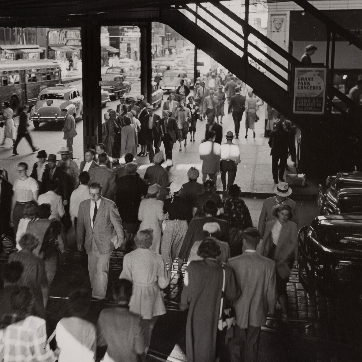 Black and white photo of crowds passing under el station in downtown Chicago