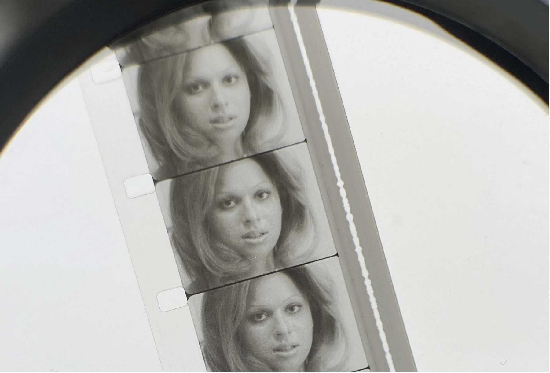 Part of a 16mm film reel viewed through a magnifier shows a woman's face in black and white