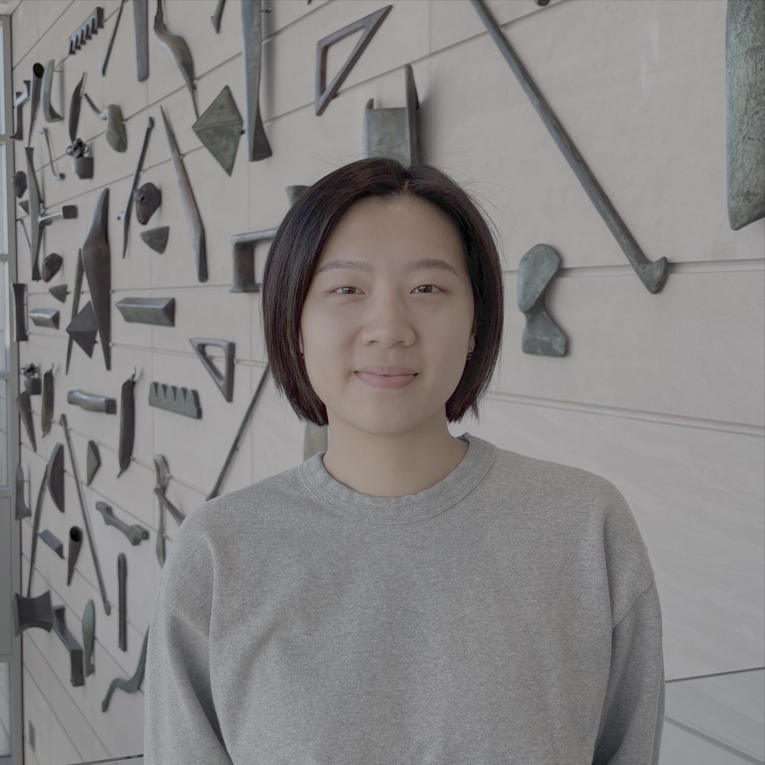 girl in grey sweater stands in front of sculpture wall in block atrium